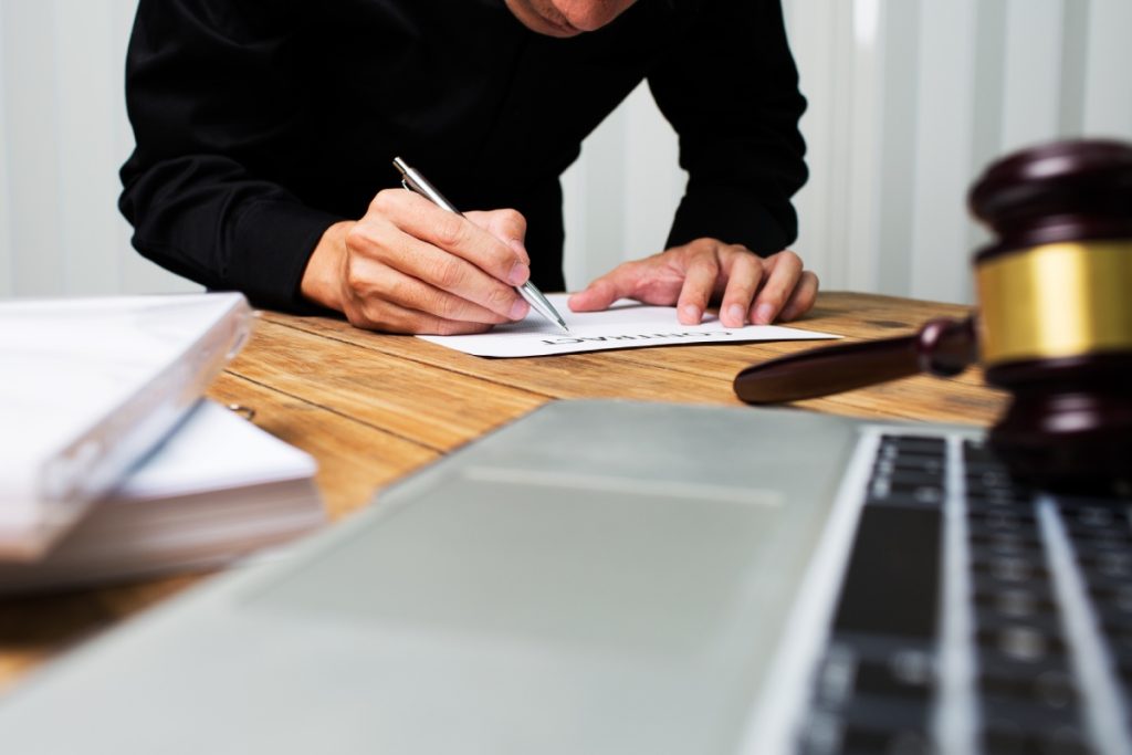 Legal professional writing on the table where there's a gavel placed on a laptop